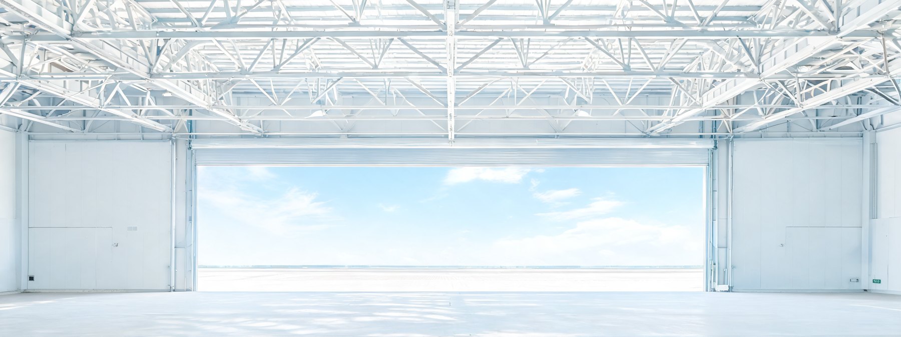 A vast empty logistics hangar at dusk, doors open to the hard-standing.